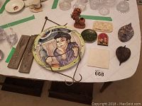 Full set of assorted decorative items including signed wall plate, Italian pottery figurine, wooden plaques, small plates, and other decor pieces on a table with grid-patterned cloth.