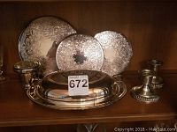 11-inch covered silver plate serving dish with two candlesticks, three patterned trivets/hot plates, and a bud frog flower arranger displayed on shelf.