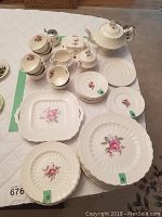 Overview of all pieces arranged on table including plates, cups, saucers, teapot, cream pitcher, sugar bowl, butter dish, serving platter.