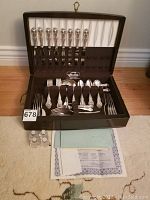 Full view of open wooden chest showing eight place settings and accessories on top of carpet