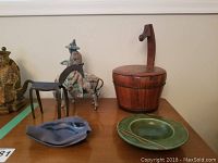 Overview photo showing five items on wood surface: wooden lidded container, metal man on horse sculpture, green ceramic plate, blue ceramic ashtray, and abstract blue ceramic piece.