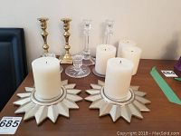 Photo showing an assortment of candles and various styles of candle holders arranged on a wooden surface.