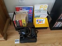 Wide view of the binoculars, books including Greater Vancouver Rand McNally, and yellow organizer with maps grouped on shelf.
