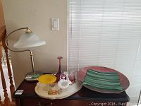 Wide shot of all items grouped on a table including Robert Held art glass pieces, Fenton glass basket, lamp, and various decorative glass items.