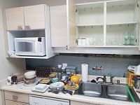 Wide shot of countertop and cabinets filled with assorted kitchen items including egg holders, bowls, plates, glasses, teapot, and microwave.