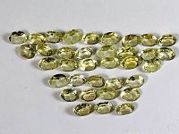 Top view displaying all 35 oval lemon citrine gemstones arranged in rows on a white background, showing facets and color.