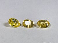 Three oval-shaped yellow sapphires arranged horizontally on a white background, showing the facets and color.