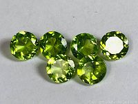 Photo of six round faceted green Peridot gemstones arranged in a row showing color and cut.
