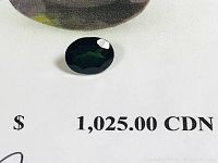 Close-up photo of the green oval Tourmaline gemstone showing its facets and dark green color on a white background with appraisal text visible in the corner.