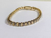 Photo of gold plated tennis bracelet laid flat, showing the stone set design and clasp.