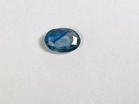 Oval faceted bi-color citrine gemstone showing blue and green hues on white background.