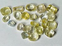 Lot of 24 unheated light yellow sapphires from Ceylon arranged on a white background showing various shapes and sizes with visible inclusions.