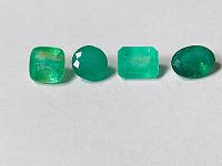 Photo showing four loose emerald gemstones laid in a row, clearly displaying different cuts and green shades with visible inclusions.