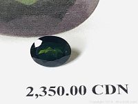 Oval cut natural green tourmaline gemstone placed on a white background with visible text indicating appraisal retail replacement value of 2,350 CAD.