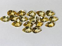 Photo showing all 17 pear-shaped yellow citrine gemstones arranged on white background.