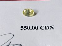 Photo of natural yellow sapphire stone on a white background showing size and color with appraisal certificate text visible.