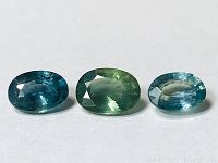 Three oval-cut sapphires in green and blue colors on a white background showing facets and size.