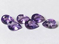 Six purple amethyst gemstones arranged in a group showing color and cut.