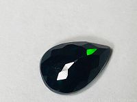 Top view of faceted pear-shaped black opal showing dark body tone with green flash