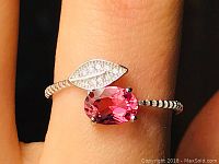 Close-up front view of adjustable sterling silver ring with pink oval tourmaline and CZ leaf accent on a finger.