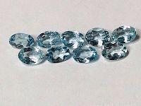 Ten oval deep blue aquamarine stones arranged in two rows showing clarity and faceting.
