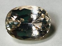 Close-up photo of oval cut faceted Kunzite gemstone showing transparent, very light yellowish pink color and facet details.