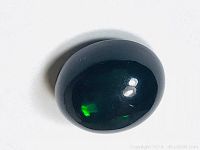 Image of the polished oval black Ethiopian opal showing its dark base color with green color flashes under bright lighting.