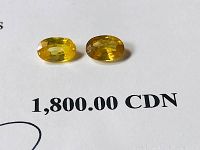 Two oval yellow sapphire gemstones displayed on white background with printed appraisal value text $1,800 CAD.