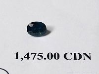 Close-up of blue oval mixed cut sapphire sitting on appraisal document showing value CAD 1,475.