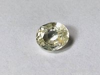 Oval faceted light yellow sapphire displayed from top-down, showing clarity and light yellow hue with visible internal inclusions.