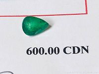 Close-up of the pear-shaped emerald on a white paper showing the price of $600 CAD reflecting retail replacement value.