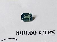 Close-up photo of the natural green sapphire gemstone showing its rectangular radiant mixed cut and deep green color.