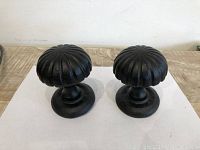 Pair of large black iron door knobs viewed from front showing rounded, ribbed design and oval base plates.