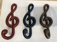 Photo of three cast iron treble clef musical note hooks in red, navy, and brown/gold, arranged side by side.