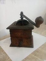Front angle view of vintage Moroccan wooden spice grinder with metal crank and drawer.