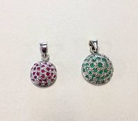 Photo showing two circular sterling silver pendants, one smaller with red ruby and cubic zirconia stones, one larger with green emerald and cubic zirconia stones.