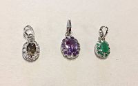 Photo of three oval-shaped sterling silver pendants with topaz, amethyst, and emerald center stones surrounded by cubic zirconia on white background.