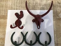Photo of three animal and horseshoe themed cast iron wall hooks arranged on wooden surface and white paper.
