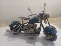 Front and side view of blue metal motorcycle figurine showing detailed engine and two front headlamps.