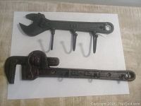 Two cast iron hooks placed on white paper, one shaped like adjustable wrench with 3 hooks the other like pipe wrench with 4 hooks.