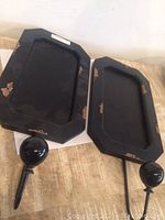 Two rectangular black chalkboards with attached glossy black hooks, showing edges with some paint wear for a rustic look, lying on a tan surface.