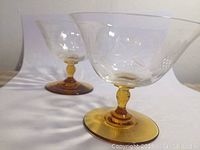 Two clear stemmed glasses with yellow bases and etched cornflower designs, arranged on a white surface.