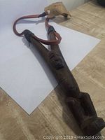 Front view of the carved wooden slingshot showing the full length with carved figure and attached leather bands and pouch.