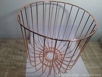 Front view of rose gold plated metal wire fruit bowl on wooden surface, showing open tall cylindrical design with vertical wire bars.