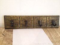 Front view of wooden and brass carved hook rack, showing detailed floral patterns and 4 brass hooks on the board.