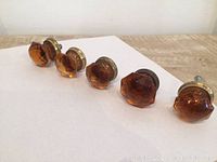 Five burnt orange glass diamond-cut mushroom-shaped cabinet knobs on a wooden surface, one knob is larger than the others