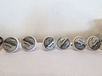 Photo showing the full set of 6 round ceramic cabinet knobs arranged in a row, each featuring the "Home Sweet Home" phrase in black script on white background.