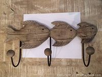Front view of wooden fish hook rack showing three fish and three hooks.