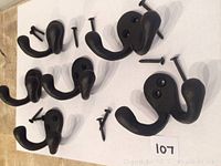 Six black metal double hooks arranged on a white surface, each with two screws included.