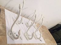 Four white metal hat and coat hooks mounted on a wooden board, showing their design and condition.